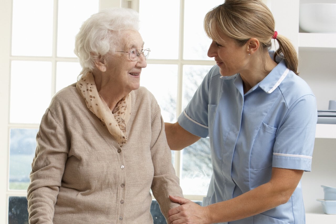 Pflegekraft im Gespräch mit einer Seniorin am Fenster